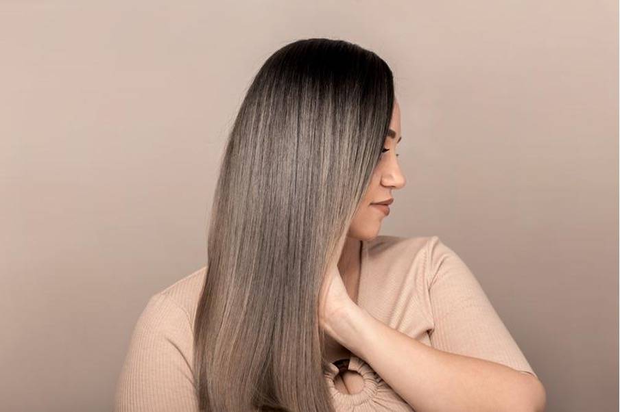 Femme aux cheveux lisses et brillants, tenant une bouteille d'huile naturelle